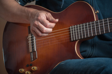 Man playing on classic guitar against silver background. Handsome young men playing guitar