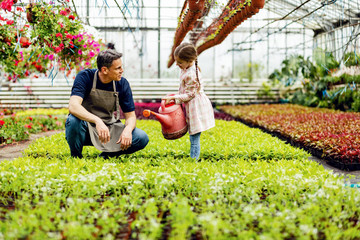 Happy little girl and her father watering plants at garden center.