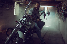 Handsome Brutal Man With A Beard Sitting On A Motorcycle In His Garage, Wiping His Hands And Looking To The Side