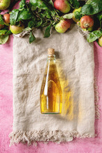 Bottle Of Fresh Apple Juice On Linen Cloth With Garden Apples With Leaves And Branches Over Pink Texture Background. Flat Lay, Space. Autumn Home Harvesting.