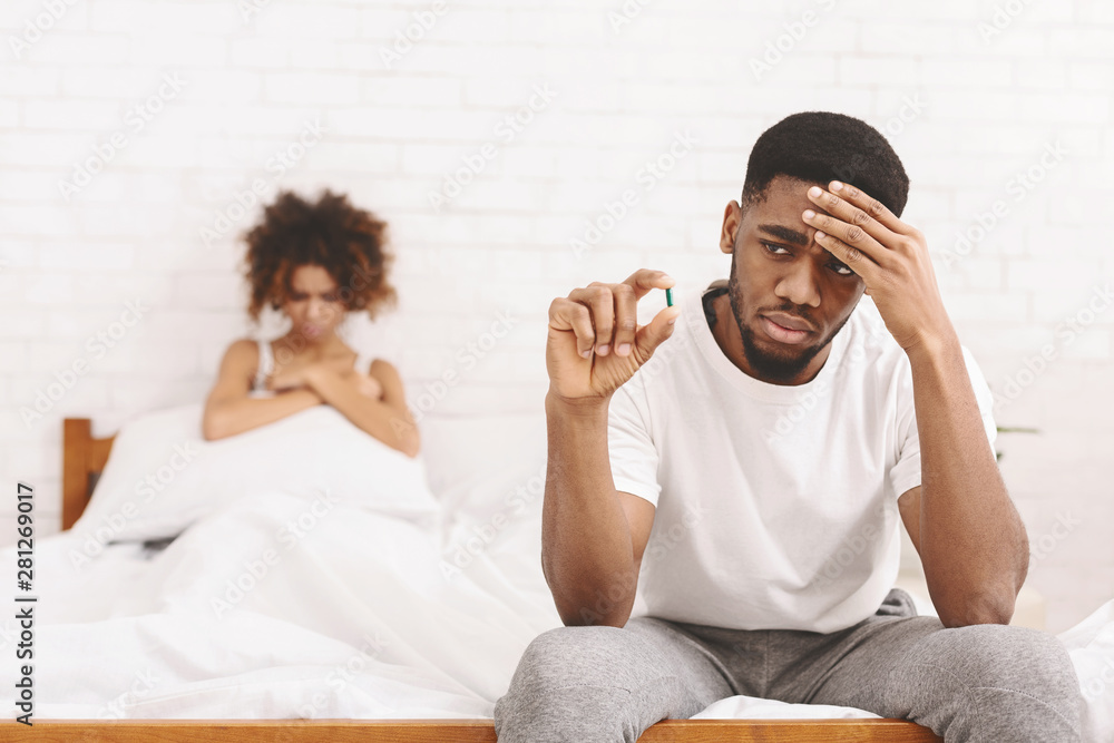 Upset black guy taking potency pill before sex with girlfriend - obrazy, fototapety, plakaty 