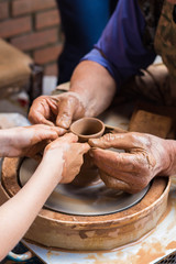 an adult potter helps a child to learn how to work with clay on a potter's wheel, forming a clay jug together