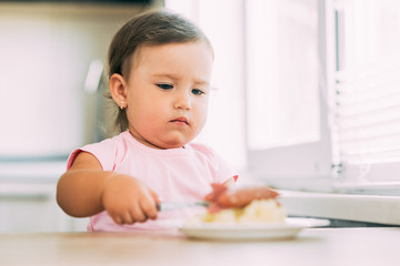 Wall Mural - Little baby girl in the kitchen eating sausage and mashed potatoes