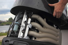 A Man's Hand Closes The Hood Of A Powerful Outboard Boat Motor, Repair And Maintenance Of Boat Engines, A View Of The Intake Manifold Of A Four-cylinder Four-stroke Injector Motor
