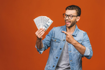 Image of shocked excited young handsome bearded man posing isolated over orange wall background holding money make winner gesture.