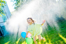 Little Girl Having Fun With Lawn Sprinkler In The Garden