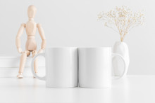 Two White Mugs Mockup With Books, Manikin And A Gypsophila In A Vase On A White Table.