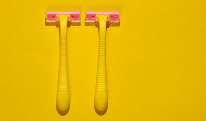 Two plastic razors on yellow background. Minimalistic beauty and fashion concept