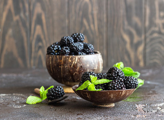 Wooden plate with ripe blackberries and mint leaves. Dark brown stone background.