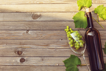 Bottle of wine with a glass and grapes on a wooden table with copy space, top view. Concept of the wine industry