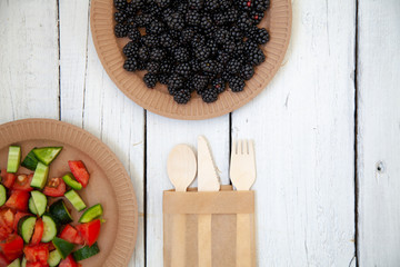 Wall Mural - paper cardboard dishes with vegetable salad tomatoes cucumbers with wooden devices fork horse knife on a white wooden table