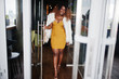 © AS Photo Family - Glamour african american woman in yellow dress and white woolen cape with handbag posed at glass door entrance of restaurant.