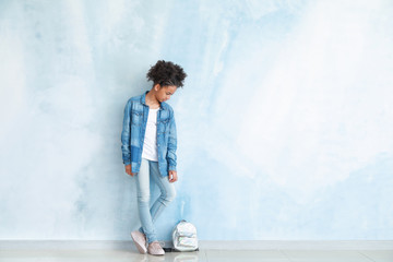 Wall Mural - Stylish African-American girl in jeans clothes and with backpack near color wall