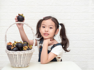 Asian little cute girl and mangosteens (Garcinia mangostana) in the wooden basket on white background. Mangosteens is a queen of fruits in thailand and very delicious.