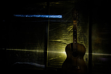 Wall Mural - An wooden acoustic guitar is against a grunge textured wall. The room is dark with a spotlight for your copyspace.