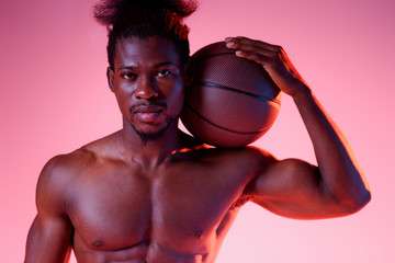 Wall Mural - confident, shirtless african american basketball player holding ball and looking at camera on pink background with gradient