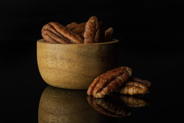 Lot of whole fresh brown pecan nut half two is near in a wooden bowl isolated on black glass