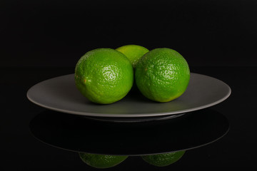 Group of three whole fresh green lime on a ceramic grey plate isolated on black glass