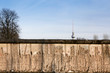 Berlin Wall original weathered section damaged with exposed iron bars partly covering the TV tower (Berliner Fernsehturm) far in the horizon.
