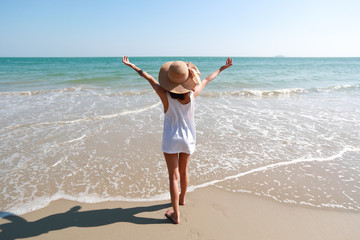 Back view portrait of sexy young girl on tropical beach with hands up while standing on sandy beach in nature with blue sky.