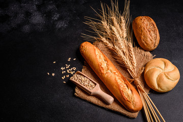 Fresh fragrant bread with grains and cones of wheat against a dark background. Assortment of baked bread on wooden table background. Fresh fragrant bread on the table