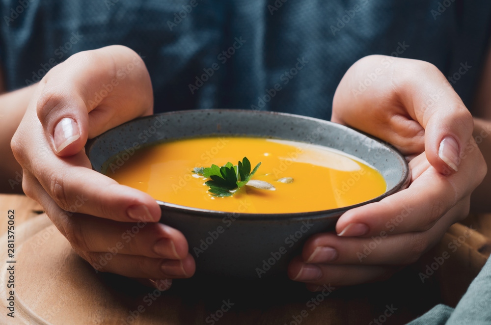 Female hand holding a  bowl with pumpkin cream soup. Cozy comfort concept. - obrazy, fototapety, plakaty 