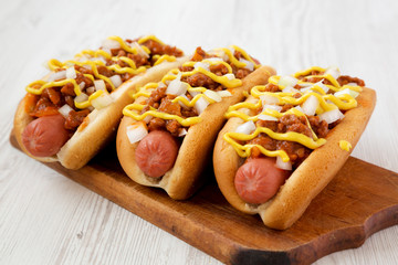 Homemade Coney Island hot dog on a rustic wooden board on a white wooden surface, side view. Close-up.