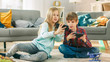 © Gorodenkoff - At Home Sitting on a Carpet: Cute Little Girl and Sweet Boy Playing in Competitive Video Game on two Smartphones, Holding them in Horizontal Landscape Mode. Girl Wins and Shows Phone to His Friend.