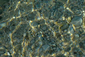 Wall Mural - Top view of blue, green and turquoise colors of water, surface of sea on rocks and bottom. Reflection of sun beams in water, shallow soil, shoal of ocean. Sea texture, background, pattern, wallpaper.