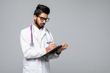 Wall Mural - Young indian man doctor with stethoscope over neck holding clipboard isolated on white