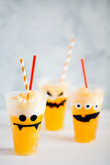 Decorated glasses with cold pumpkin orange cocktail(punch,lemonade,shake,smoothie) with cute,funny and spooky face for Halloween with copy space for text.Ideas handcraft  for a children's party.DIY