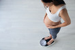 Pretty young pregnant woman standing on scales at home.