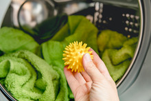 Using Pvc Dryer Balls Is Natural Alternative To Both Dryer Sheets And Liquid Fabric Softener, Balls Help Prevent Laundry From Clumping In The Dryer.  Woman Hand Put In A Yellow Spiky Dryer Ball.