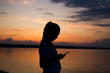 © Yuliya Timofeeva - Silhouette of a young woman on sunset background with a mobile phone in her hands