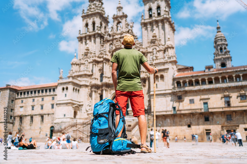 Young backpacker man pilgrim standing on the Obradeiro square (plaza) - the main square in Santiago de Compostela as a end of his Camino de Santiago pilgrimage. - obrazy, fototapety, plakaty 