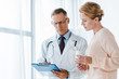 © LIGHTFIELD STUDIOS - doctor in glasses holding clipboard with pen near woman with bottle