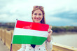 © sakkmesterke - Young redhead woman holding Hungarian flag on bridge