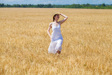 Young brunette woman in white dress walking in a wheat field