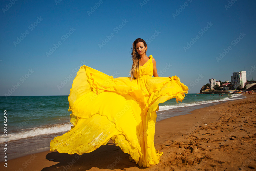 young beautiful girl walks op the sandy beach in a flying yellow dress ...