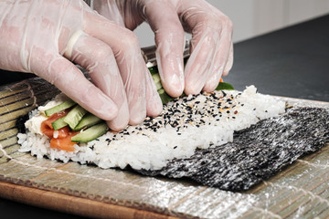 Cook's hands close-up. A male chef makes sushi and rolls from rice, red fish and avocado. White gloves.