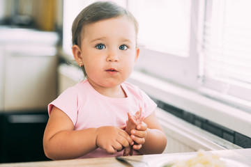 Wall Mural - Little baby girl in the kitchen eating sausage and mashed potatoes