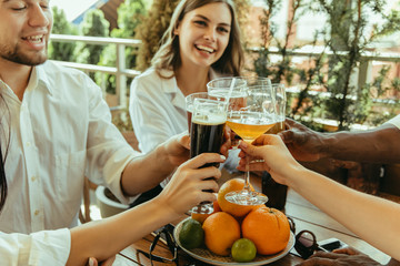 Young group of friends drinking beer, having fun, laughting and celebrating together. Women and men with beer's glasses in sunny day. Oktoberfest, friendship, togetherness, happiness, summer concept.