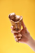 © LIGHTFIELD STUDIOS - cropped view of woman holding delicious melted chocolate ice cream in crispy waffle cone isolated on yellow