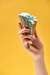 partial view of woman holding delicious melted blue ice cream in crispy waffle cone isolated on yellow