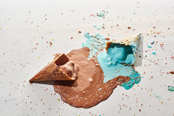 Sticker - top view of delicious melted chocolate and blue ice cream in waffle cones on marble grey background with sprinkles