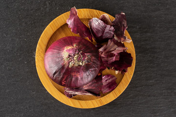 One whole lot of pieces of stale red onion on bamboo plate flatlay on grey stone