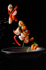 Wall Mural - close-up, Seafood, chef cooks shrimps with pepper, spiked beans and Brussels sprouts in a frying pan. On a black background for design, menus, restaurants, oriental cuisine, healthy food