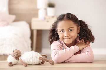 Adorable little African-American girl sitting at table