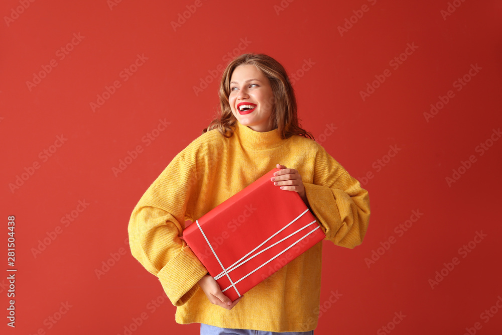 Happy young woman with Christmas gift on color background