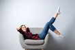 © Богдан Маліцький - young girl is sitting on a soft comfortable chair against a white wall with her legs raised up, a hipster student is resting and dreaming, copy space